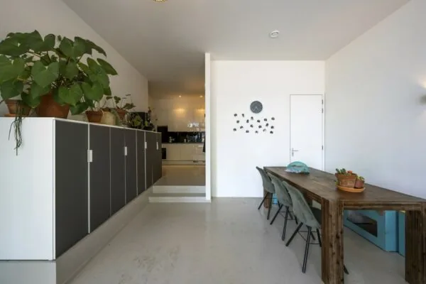 Moderne eetkamer met houten tafel, groene stoelen, kamerplanten en zicht op een open keuken aan de James Wattstraat.